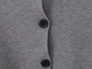 Close-up detail of grey knitted fabric texture and black button on a long sleeve cardigan