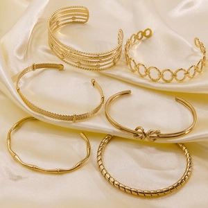 Set of six minimalist 14k gold plated titanium steel open bangles on silk background