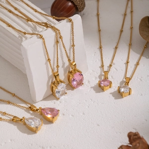 Minimalist gold necklaces with pink and white zircon drop pendants on stone display
