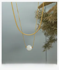 Detail of double-layer gold snake chain featuring a matte white pearl bead pendant