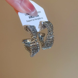 Macro shot of silver twisted C-shape hoop earrings with rich texture and mirror finish