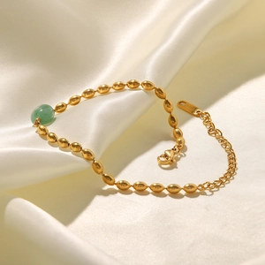Detail of gold oval bead bracelet featuring green natural stone on white silk background