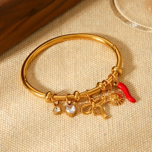 Gold open bangle with sun, chili, and bow charms on beige textured fabric background