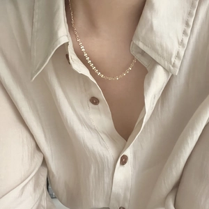 Close-up of a delicate gold minimalist link necklace worn over a silk shirt