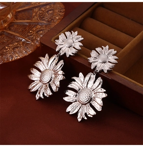 Macro shot of silver sunflower drop earrings with textured petals on a velvet jewelry box