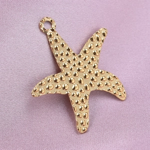 Detail of a gold starfish pendant with a hammered texture on a soft purple fabric