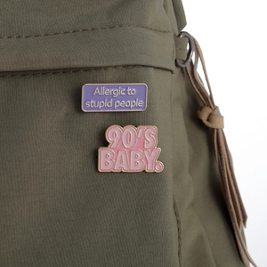 Enamel slogan pins featuring 90'S BABY and Allergic to stupid people on a green bag
