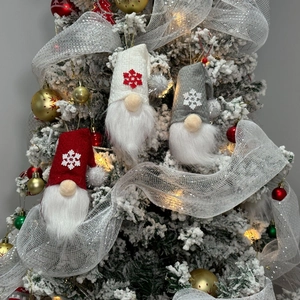 Close-up of three knitted Christmas gnome ornaments with snowflake hats on a festive tree