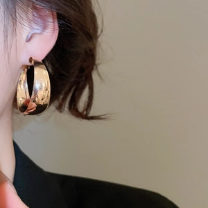Close-up of a wide polished gold crescent hoop earring worn by a model in warm light