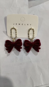 Detail of dark red velvet bow earrings with gold rhinestone oval studs and tassels