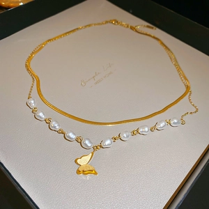 Dettaglio della collana a farfalla dorata con catena di perle e maglia a serpente