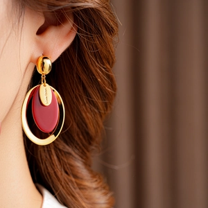 Close-up of gold plated oval earrings with red resin and hand made metal tag on model
