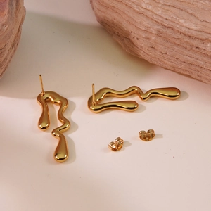 Macro shot of molten gold wavy earrings with high mirror polish on natural stone base