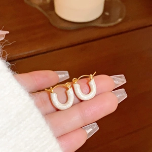 Close-up of gold U-shaped earrings with cream enamel and a clip-back closure detail