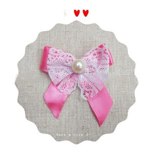 Close-up of pink satin ribbon bow with white floral lace and shiny pearl center embellishment