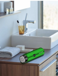 Detail view of a portable green electric shaver on a wooden bathroom vanity surface