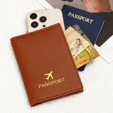 Vue à plat d'un protège-passeport marron effet paille avec avion doré et accessoires voyage