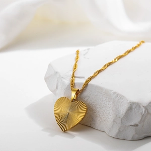 Detail of 18k gold heart necklace with radial brushed texture on white stone