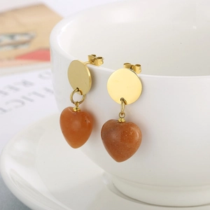 Detail of heart-shaped earrings with gold circular studs on a white ceramic cup