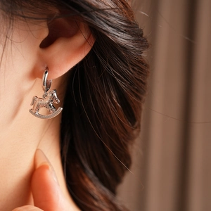 Close-up of a silver rocking horse earring worn by a model in a minimalist style