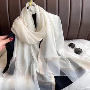Detalle de bufanda blanca transparente con rayas doradas y grises sobre blusa negra
