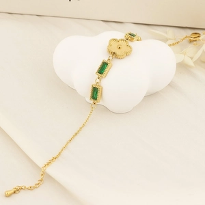 Golden stainless steel bracelet with green rectangular gems and clover charms on white stone