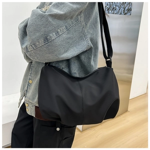Detailed side view of a large black minimalist crossbody bag worn by a model