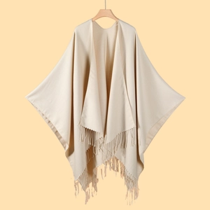 Detail of beige knitted shawl on a wooden hanger with decorative fringe finish