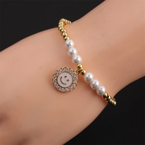 Detail of beaded bracelet featuring gold copper beads, white pearls and a zircon smiley charm