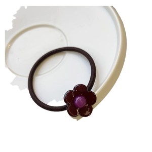 Élastique à cheveux fleur marron foncé avec perle violette sur une assiette blanche