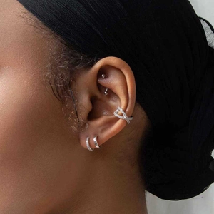 Macro detail of silver crisscross ear cuff with zircons and layered hoop earrings on model