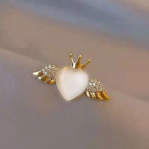 Detail of heart-shaped opal brooch with gold crown and sparkling crystal wings on fabric