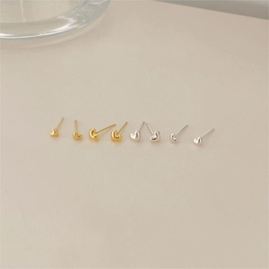 Close-up of minimalist gold and silver heart stud earrings on a neutral background