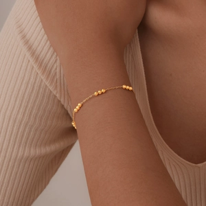 Close-up of golden stainless steel beaded bracelet on a woman's wrist in warm lighting