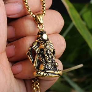 Close-up of hand holding a golden Ganesha elephant pendant on a stainless steel chain