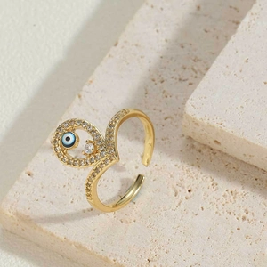 Gold evil eye open ring with white zircon stones on a minimalist beige stone background