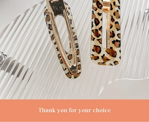 Detail of leopard print hair clips with gold metal base on a clear textured surface
