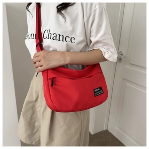 Detail of red nylon crossbody bag with adjustable strap worn by model against a white wall