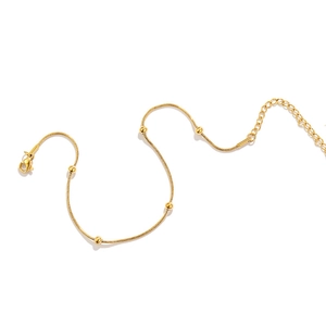 Close-up of gold snake bone chain with round bead charms and secure lobster clasp