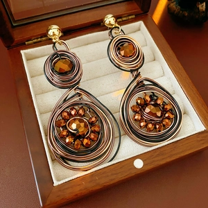 Detailed view of vintage hand-woven bronze swirl earrings with faceted beads in a wood box