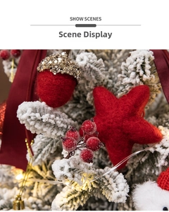 Close-up of red felt stars and acorn decorations with warm lights on snowy pine branches
