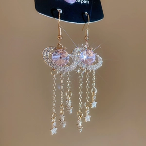 Macro view of crystal planet fringe earrings with pink stones and gold star chains
