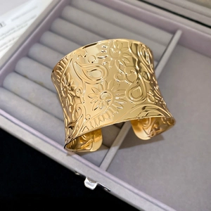 Detail view of a wide gold cuff bracelet with embossed floral and paisley patterns