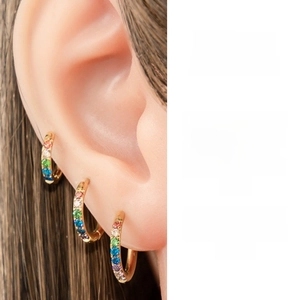 Detail of three gold hoop earrings with multi-colored zirconia stones on model's ear