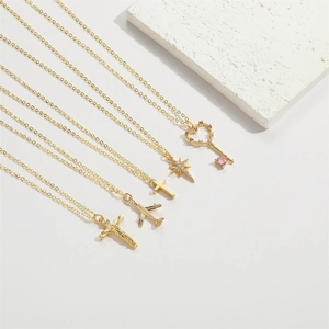 Close-up of gold plated necklaces with cross, star, and pink heart key pendants