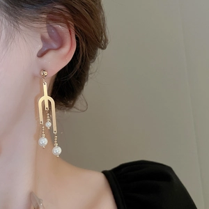 Detail of long gold U-shaped drop earrings with white pearls worn by a model
