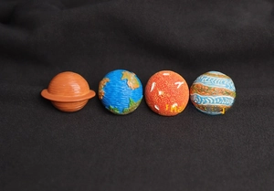 Detail view of four colorful 3D cartoon planet pins featuring Saturn, Earth, and Jupiter
