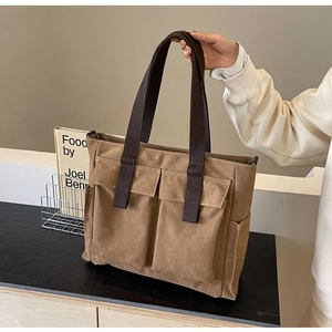 Detail of khaki canvas tote bag featuring large front pockets and brown carry handles
