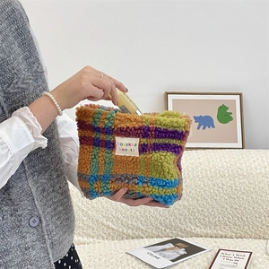 Detail of colorful plaid plush bag being filled with cosmetics in a cozy home setting