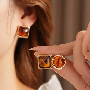 Close-up of amber resin earrings with golden metal studs worn by a model in soft lighting